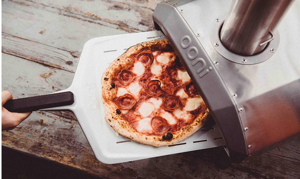 Un horno de pizzas portátil de  exterior cociendo una pizza en su interior. Marca ooni modelo jaru 12.